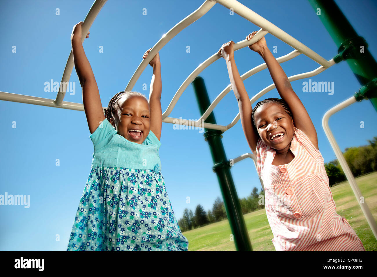 Two children hanging from monkey bars in a playground Stock Photo