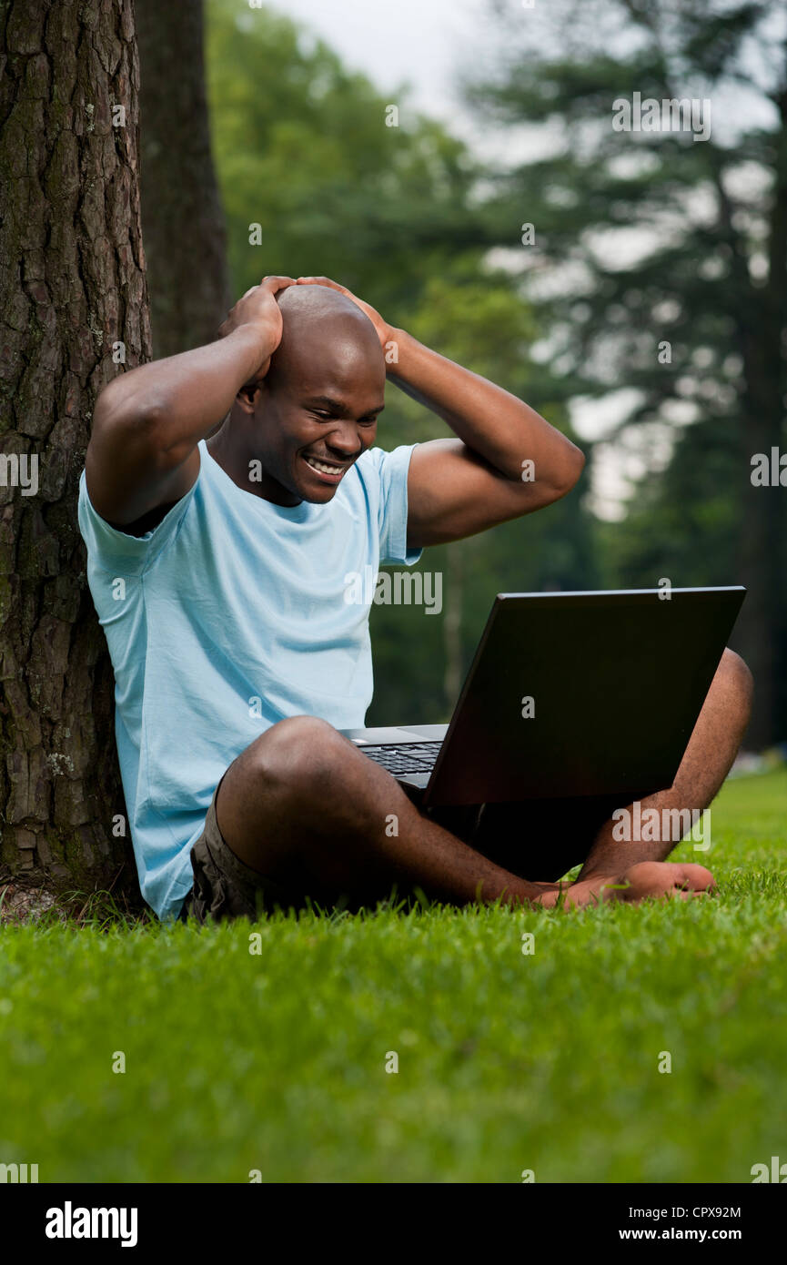 Young African man sitting in a park, working on a laptop Stock Photo ...