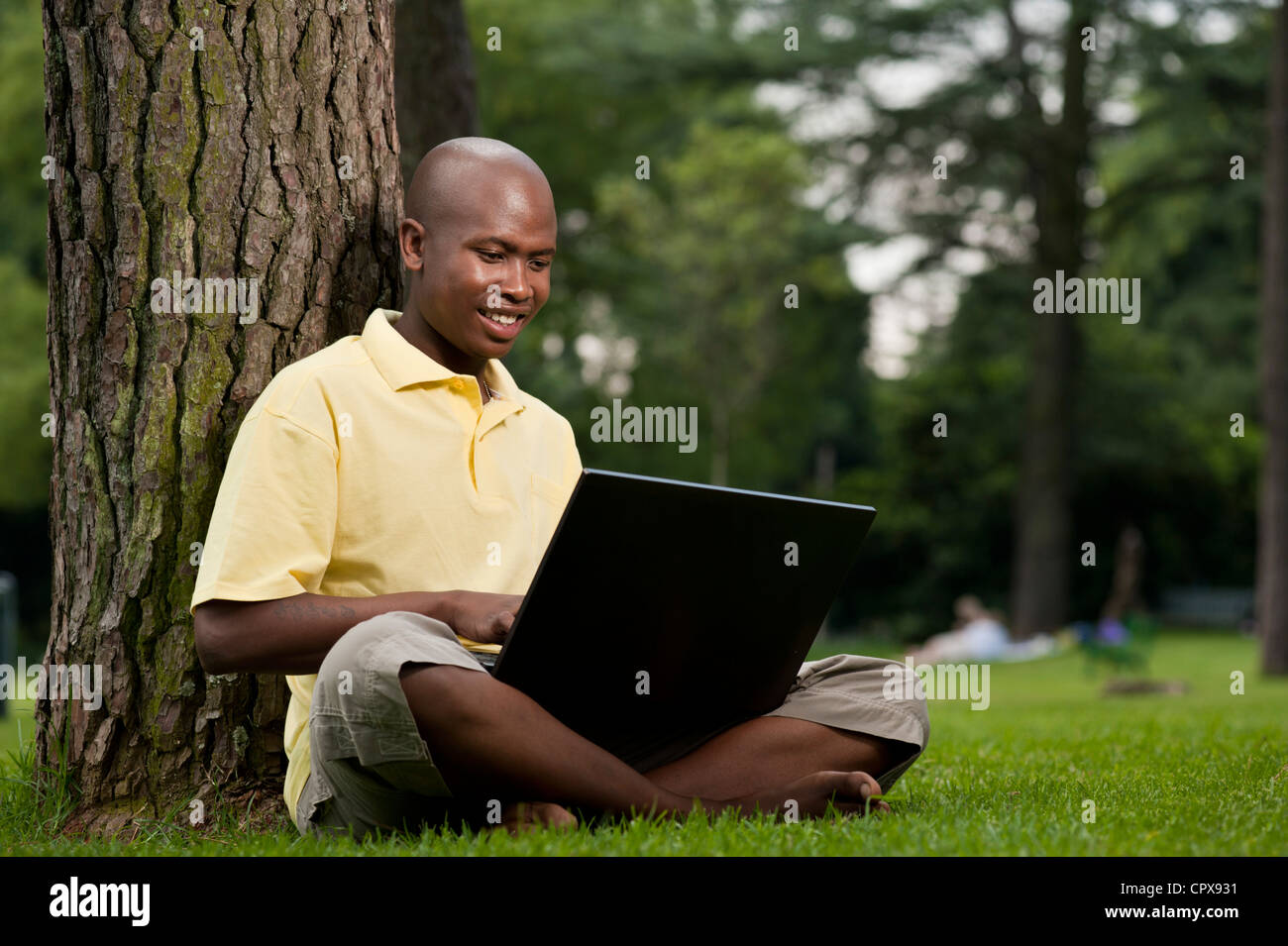 Young African man sitting in a park, working on a laptop Stock Photo ...
