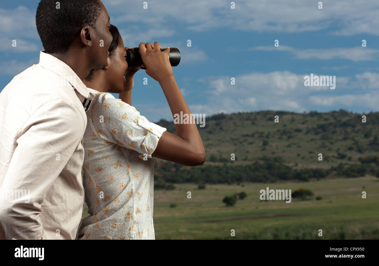An African couple searches for animals at a Game Reserve through binoculars Stock Photo