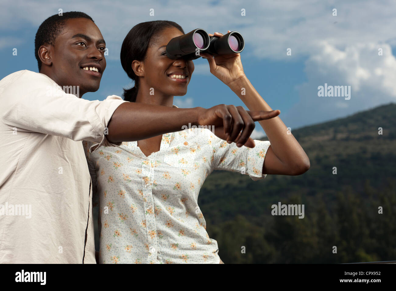 An African couple searches for animals at a Game Reserve through binoculars Stock Photo