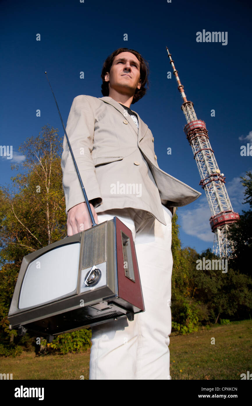 Young man holding portable retro tv set in front of high television tower Stock Photo