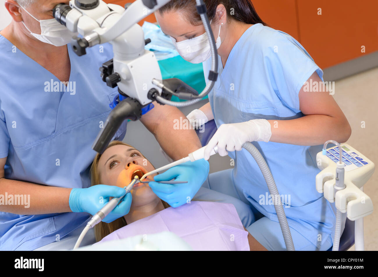 Dentist operating female patient through microscope at surgery office Stock Photo
