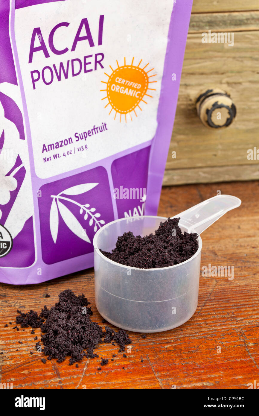 dried acai berry powder in a plastic measuring scoop against grunge wood background with the original package from Navitas Stock Photo