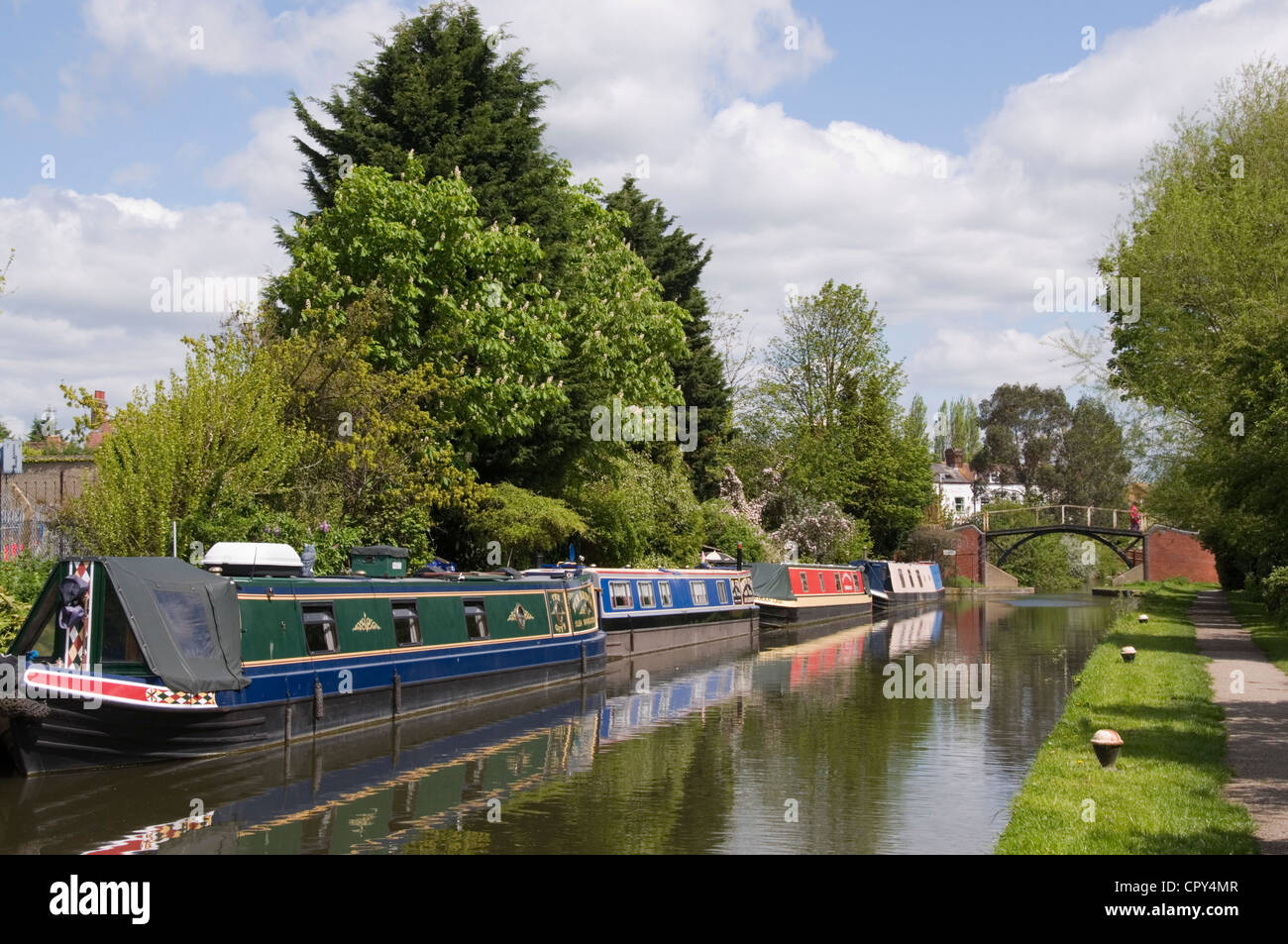 Bucks - Aylesbury Arm of GUC canal - view of the waterway - moored canal boats - distant bridge - trees - sunlight - blue sky Stock Photo