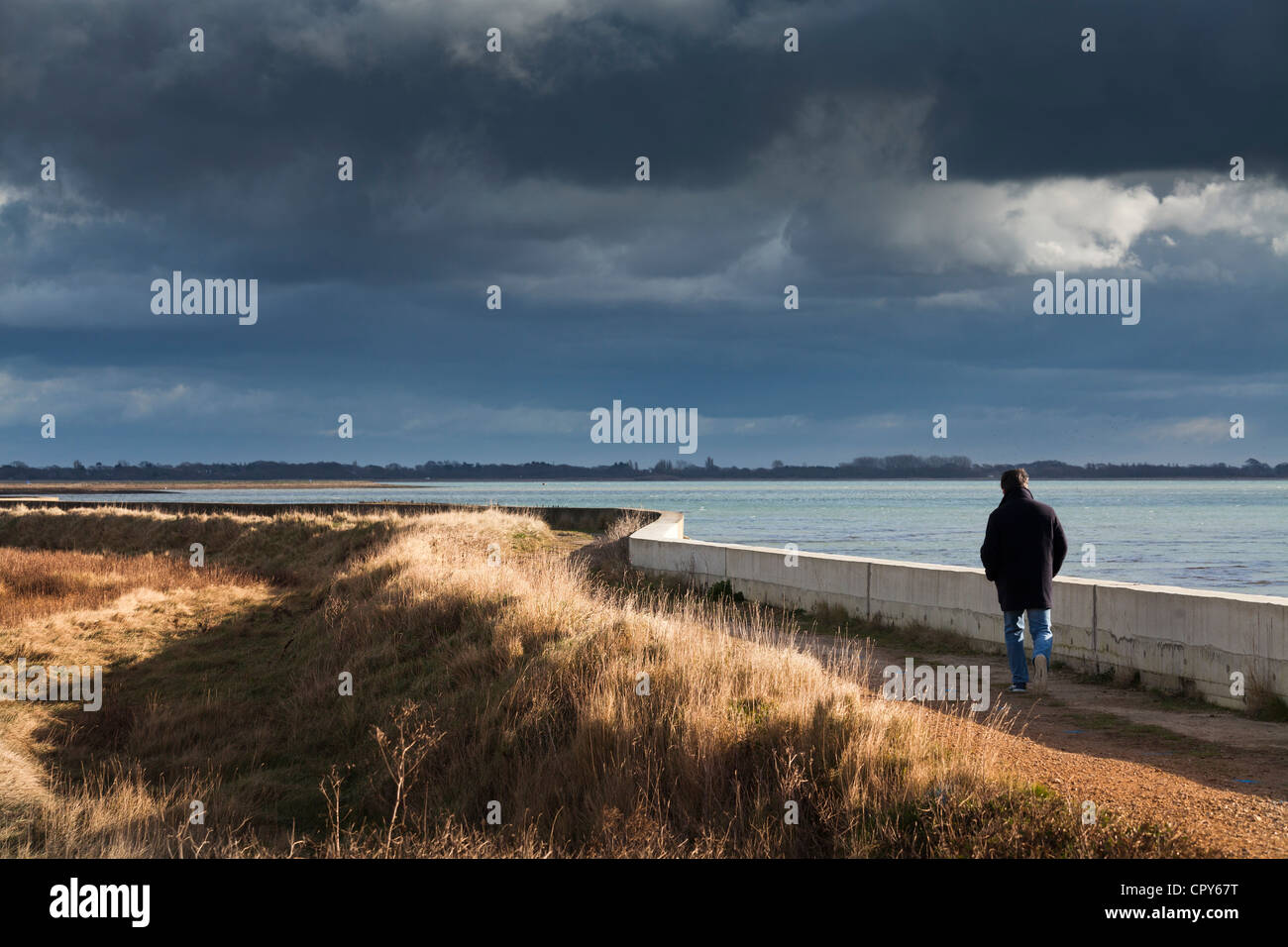one man walking alone by sea wall in sunshine on dramatic stormy day in sunshine Stock Photo