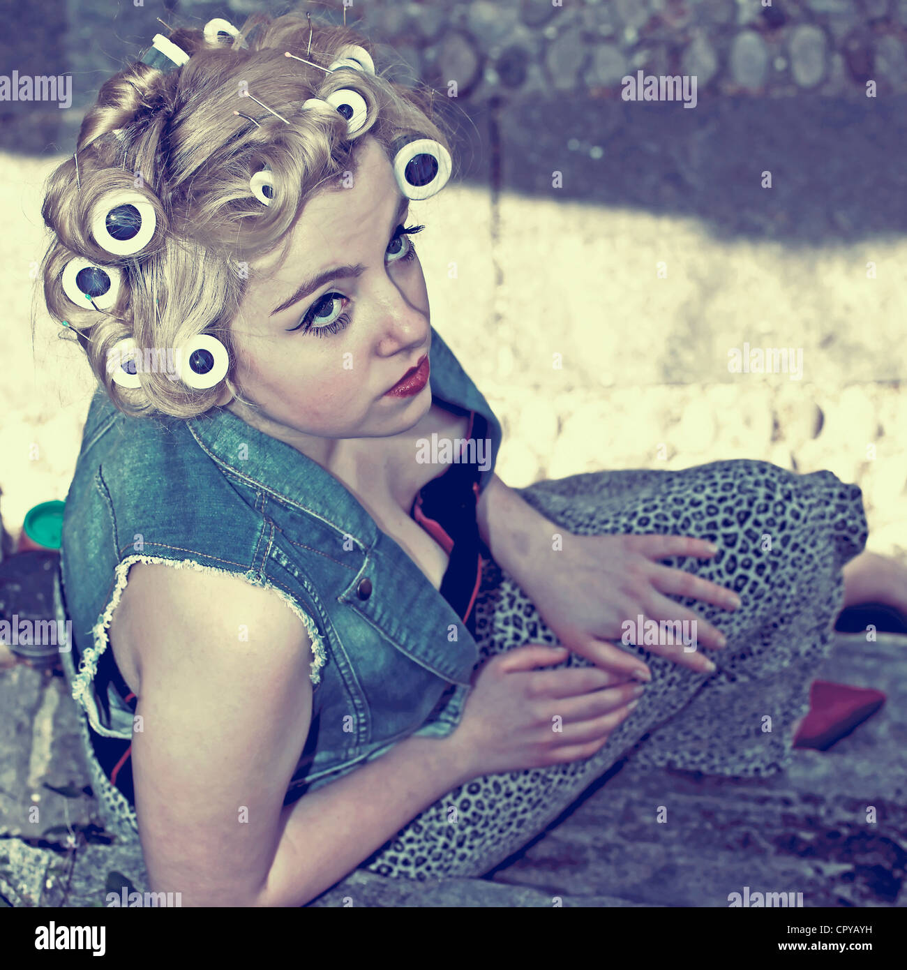 young woman with curlers sitting on a stone staircase Stock Photo