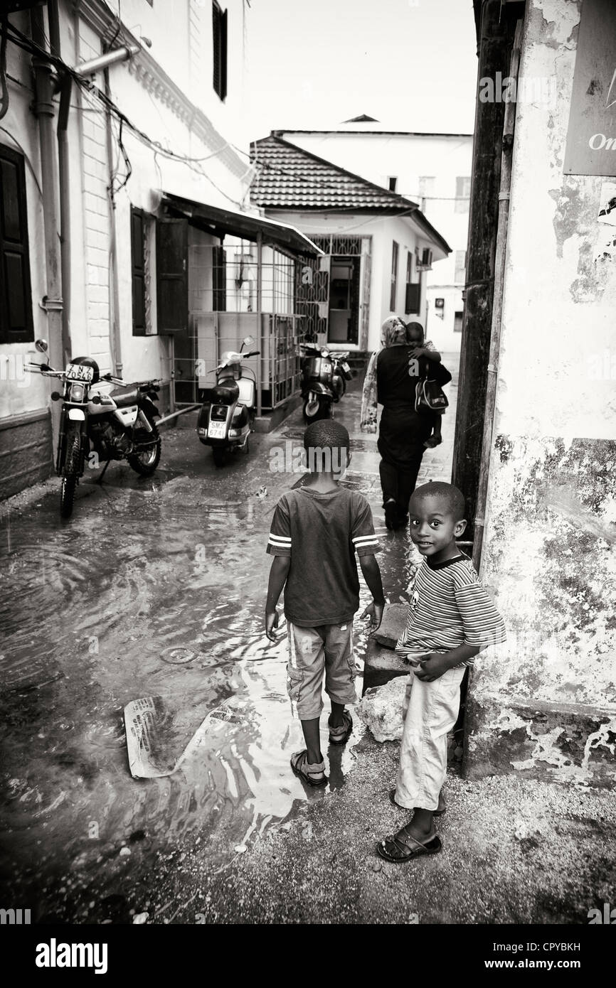 Two children contemplating crossing flooded street, Zanzibar, Africa Stock Photo