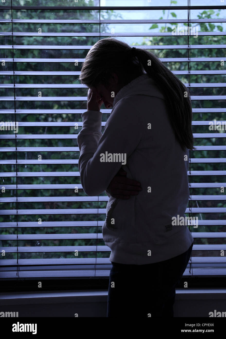 Profile of a girl with a ponytail, standing hands covering her face. Silhouette. Stock Photo