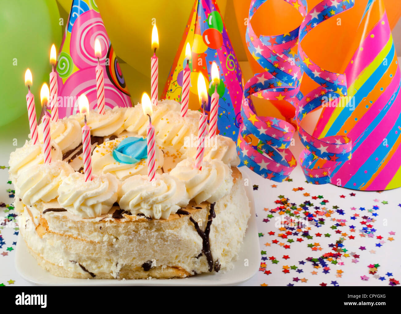 Birthday cake and candles against colorful party background with hats and serpentines Stock Photo