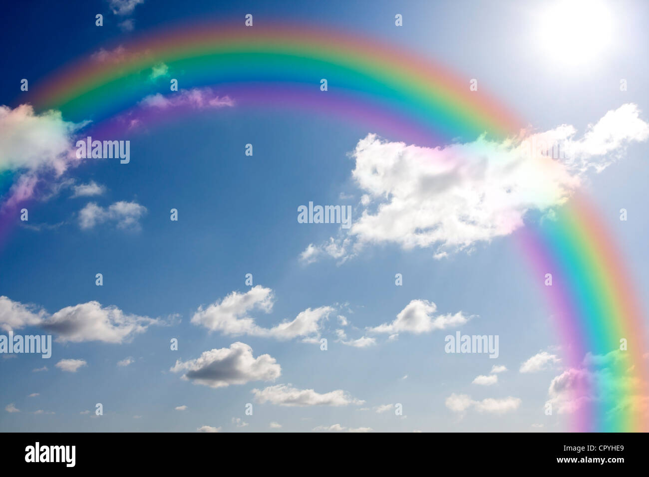 Rainbow and sun against blue sky with clouds Stock Photo