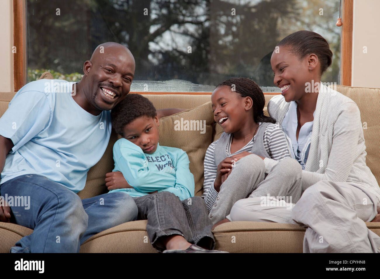 Family laughing and sitting on couch together, but son looks annoyed, Illovo Family, Johannesburg, South Africa. Stock Photo