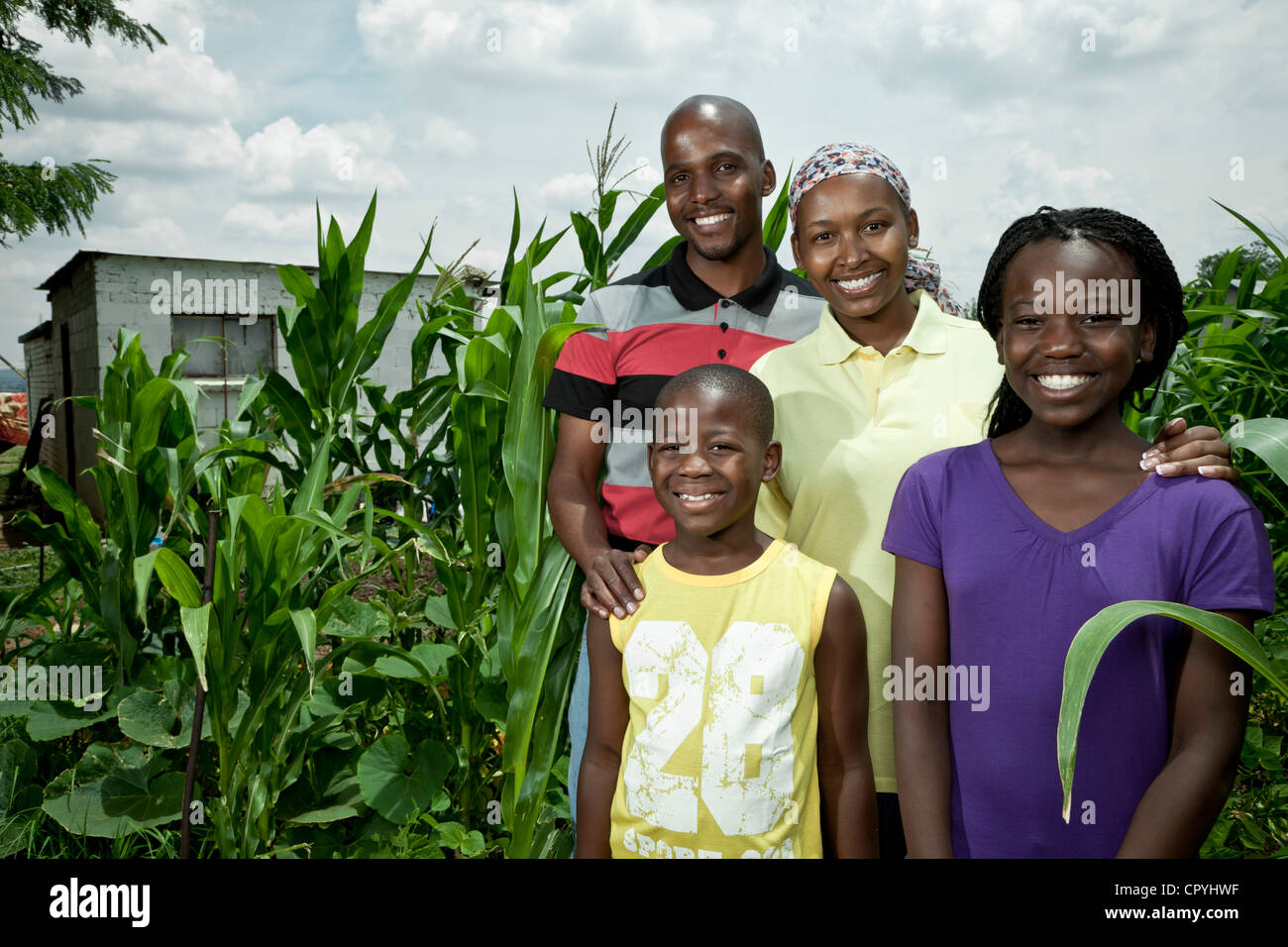 African family stands amongst some crops, smiling at camera Stock Photo