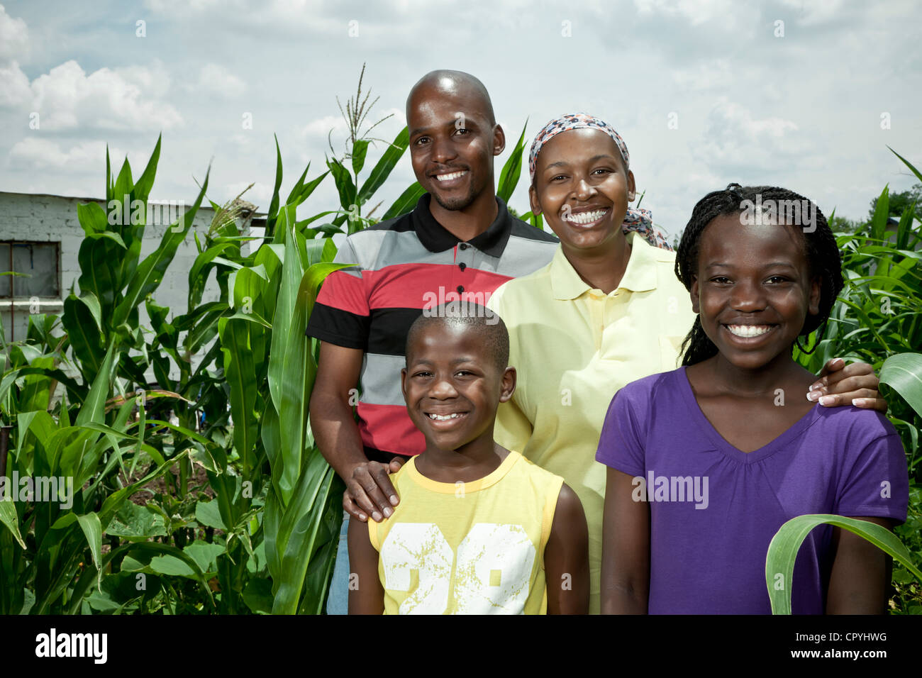African family stands amongst some crops, smiling at camera Stock Photo