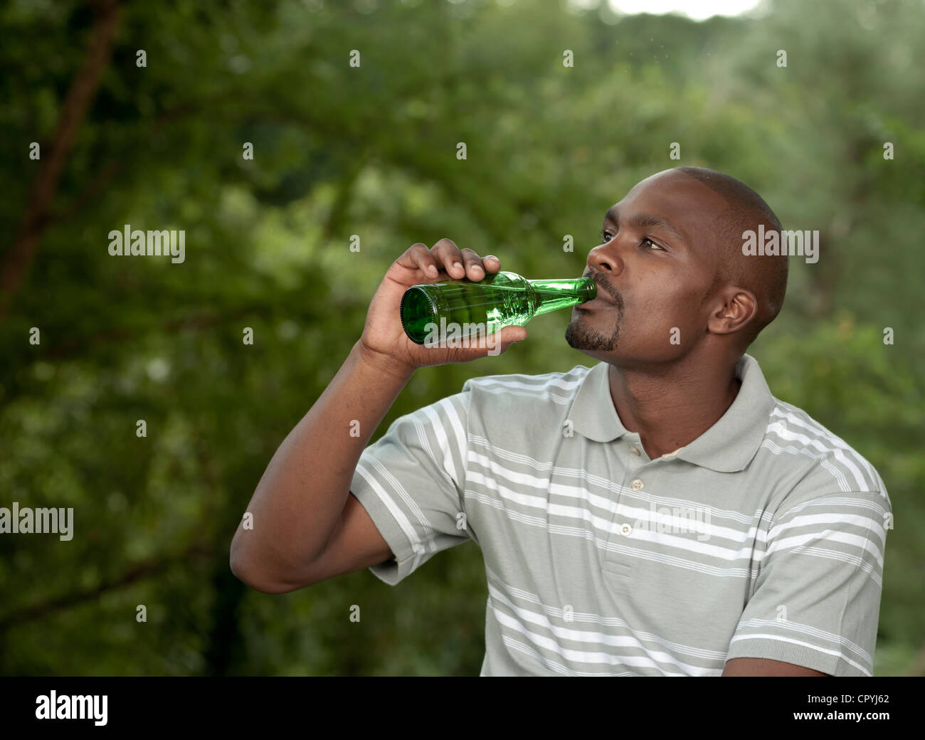 African Man sits outside drinking a beer Stock Photo