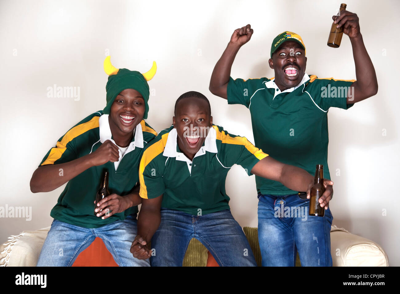Three friends dressed in rugby uniforms watch a rugby game on TV whilst