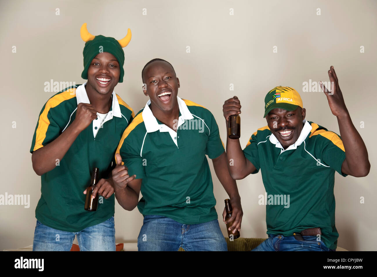 Three friends dressed in rugby uniforms watch a rugby game on TV whilst ...