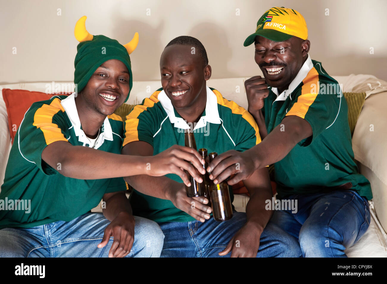 Three friends dressed in rugby uniforms watch a rugby game on TV whilst