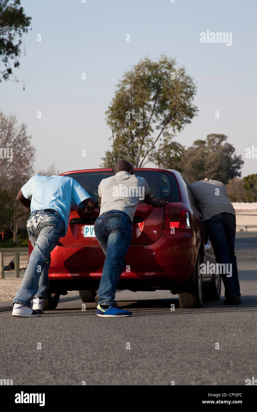 Two men pushing a car while a third steers it Stock Photo Alamy