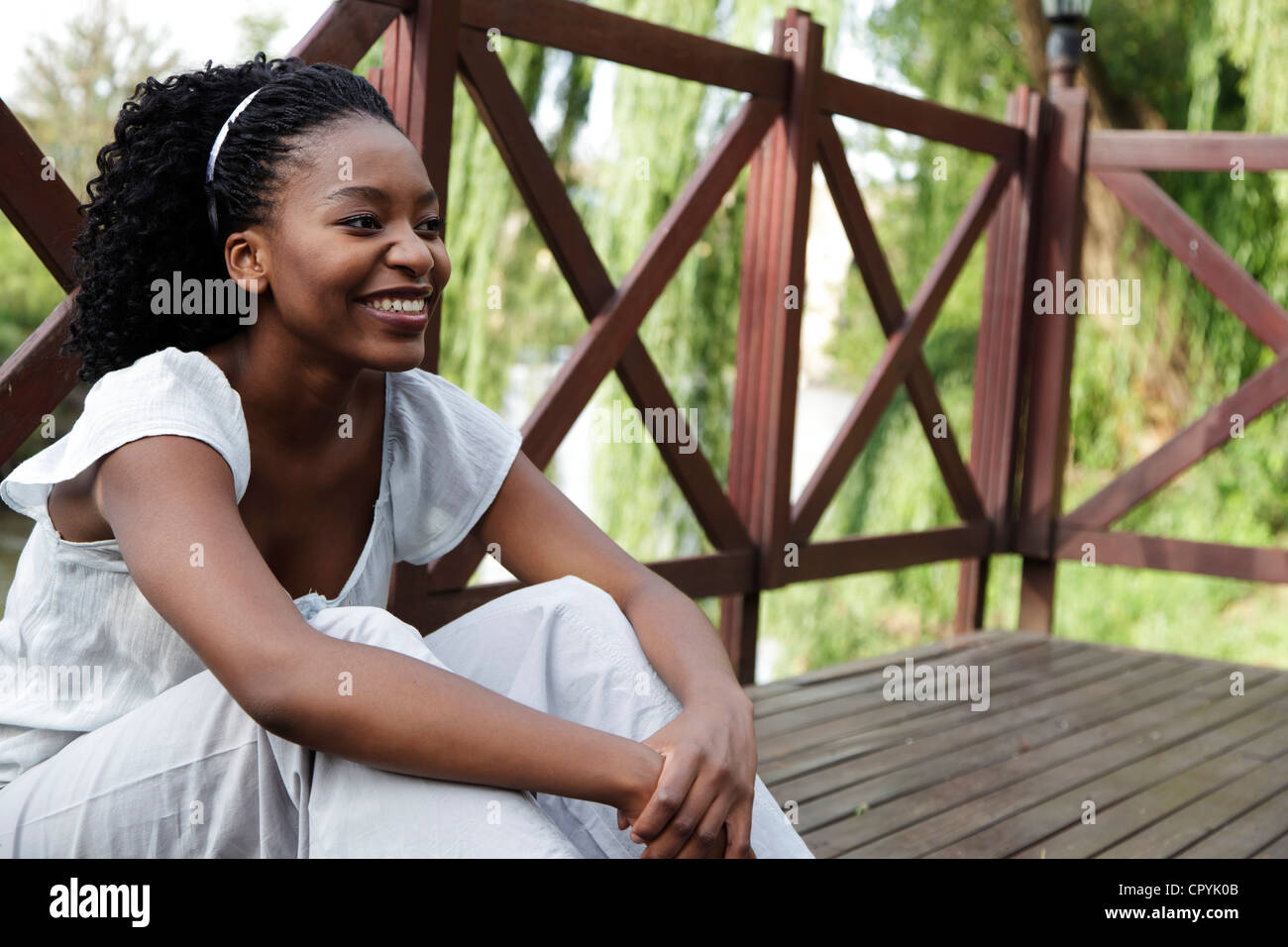 Young African woman sits on a wooden deck Stock Photo