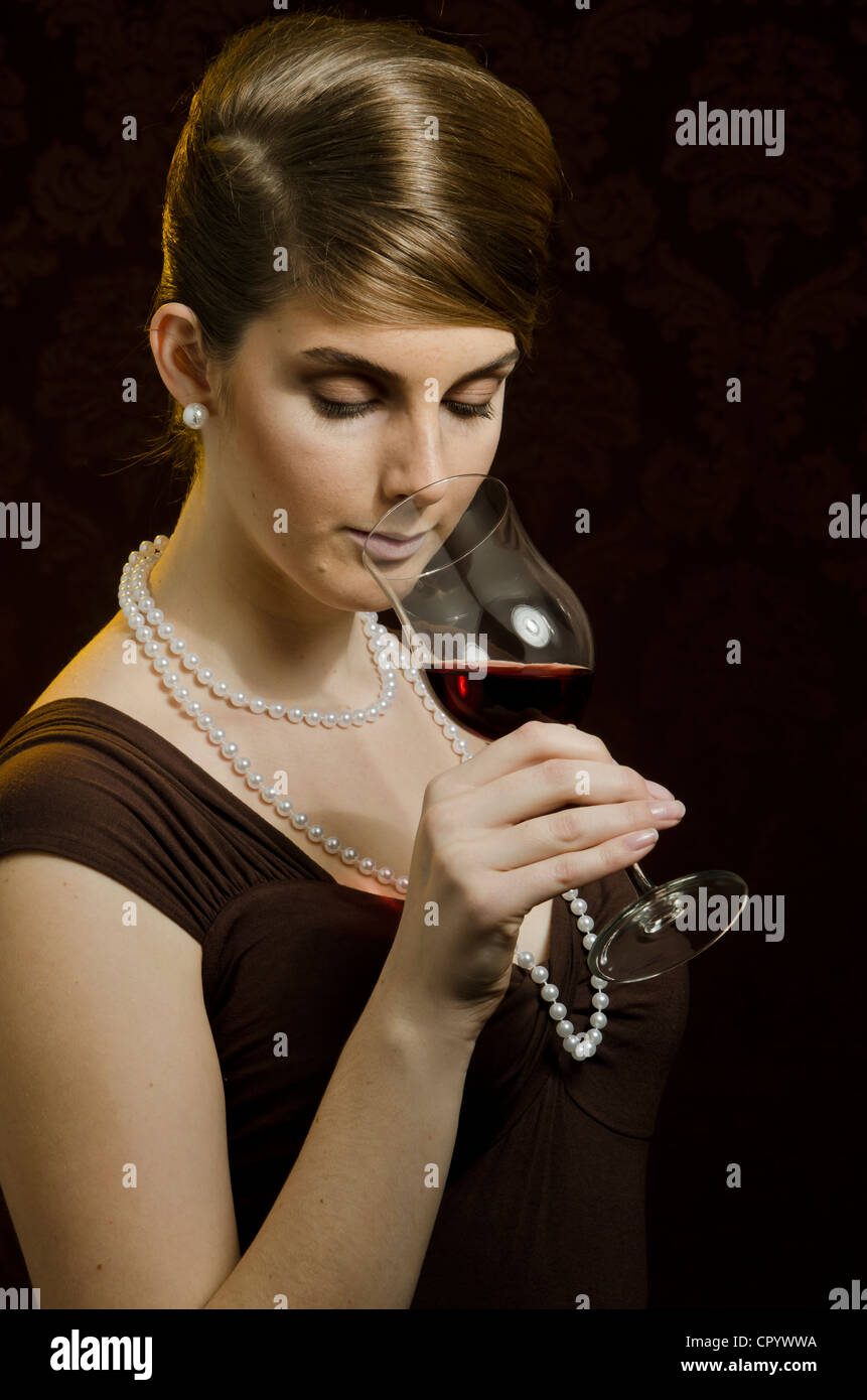 Young woman wearing a pearl necklace and pearl earrings, drinking red wine in a wine glass Stock Photo