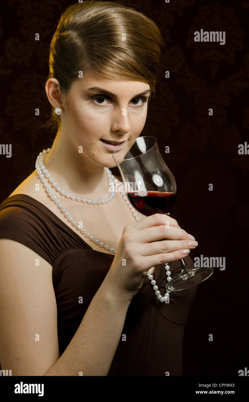 Young woman wearing a pearl necklace and pearl earrings, drinking red wine in a wine glass Stock Photo