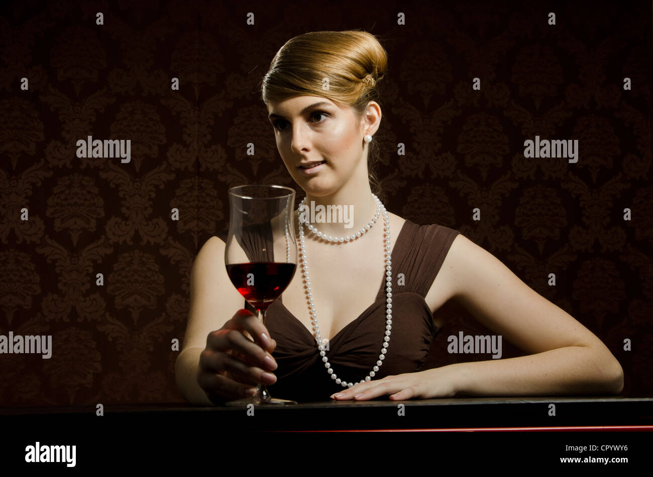 Young woman wearing a pearl necklace and pearl earrings, with red wine in a wine glass Stock Photo