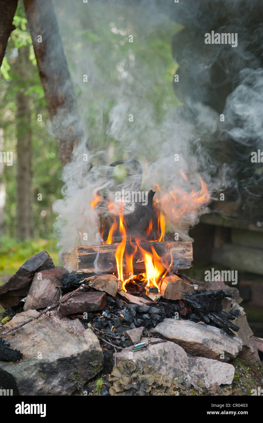 Boiling water in the wilderness, coffee kettle on a fireplace, flames and smoke, Tjaernvallen in Fulufjaellets National Park Stock Photo