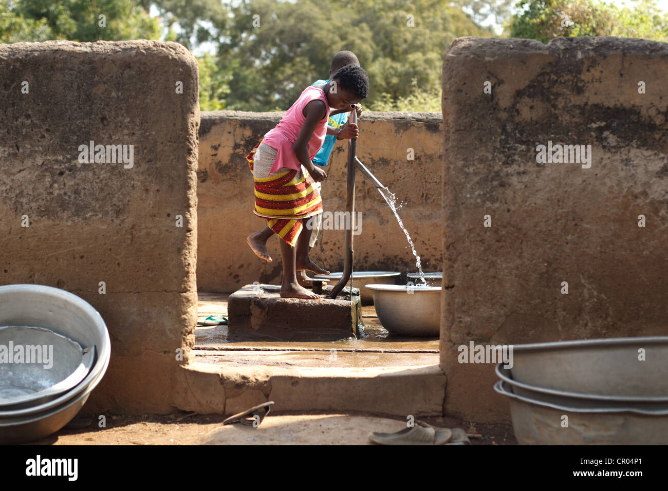 Children fill containers with water from a communal foot-activated pump in the village of Kiendi-Walogo, Zanzan region Stock Photo