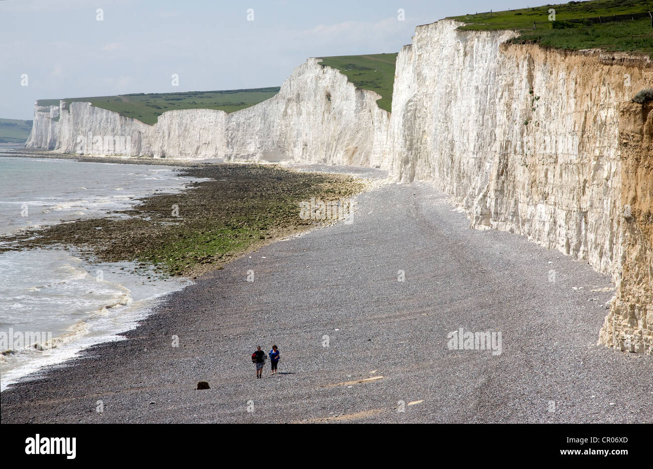 UK. England. Kent. Eastbourne. Chalk cliffs and couple walking along pebble beach. Stock Photo