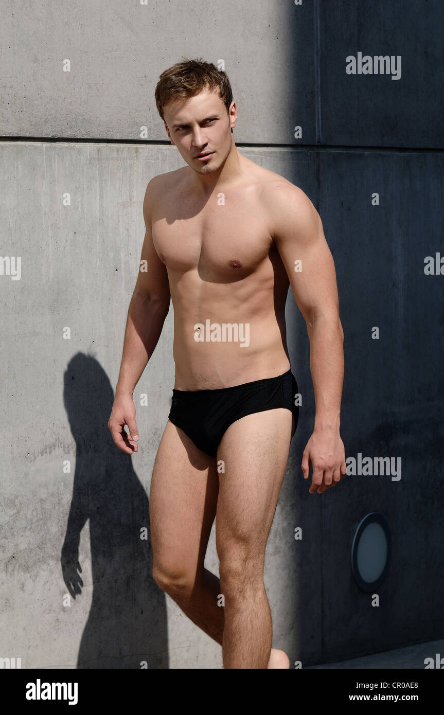 Young man wearing bathing trunks, walking in front of a concrete wall Stock Photo