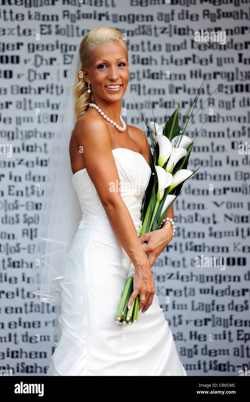 Wedding, smiling bride with bridal bouquet standing in front of a wall ...