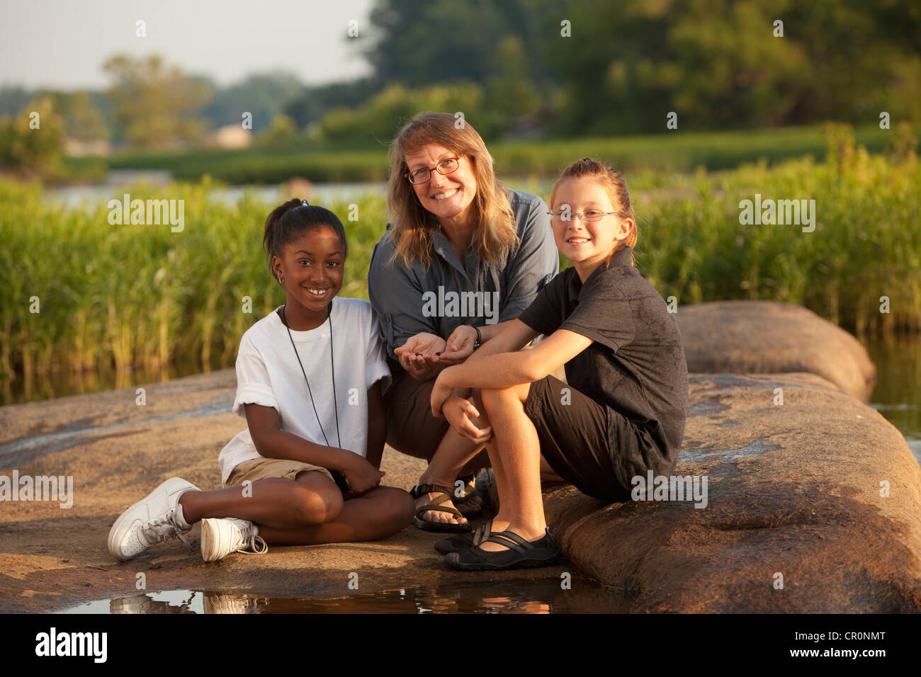 Teacher and students sitting on rock near river Stock Photo - Alamy