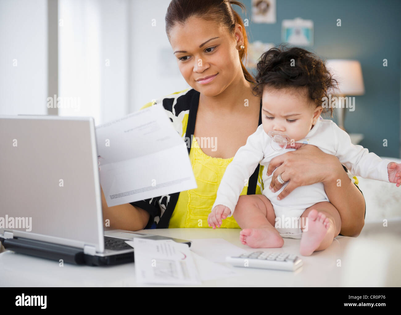 Mixed race mother holding baby and paying bills Stock Photo