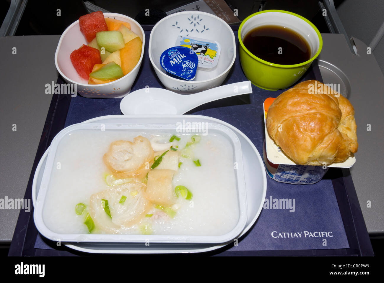In flight meal with Cathay Pacific airline: food includes a croissant, fish in butter sauce, fruit salad and a cup of coffee Stock Photo