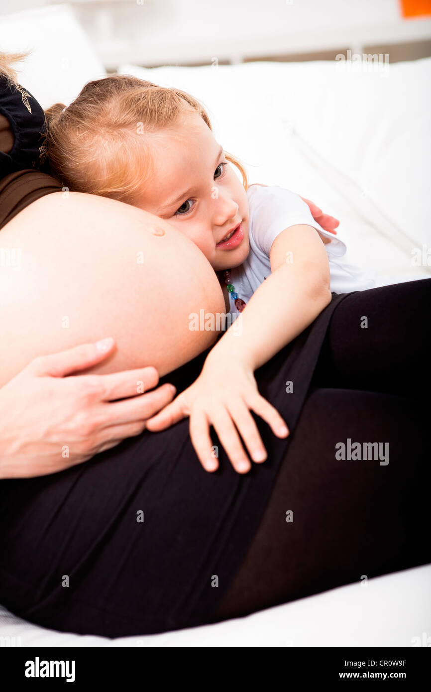 Girl listening to pregnant mother's belly Stock Photo