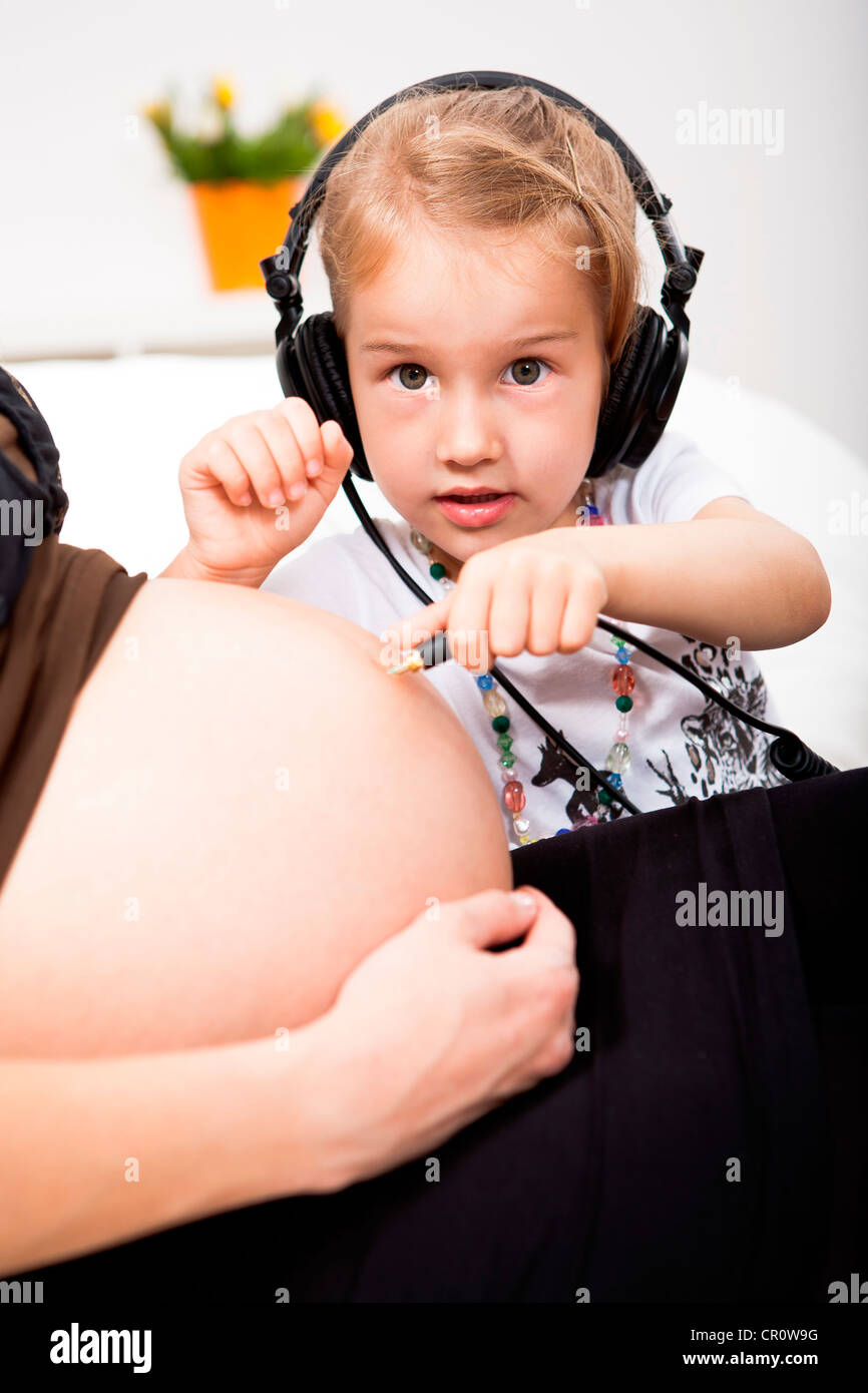 Girl with headphones listening to pregnant mother's belly Stock Photo