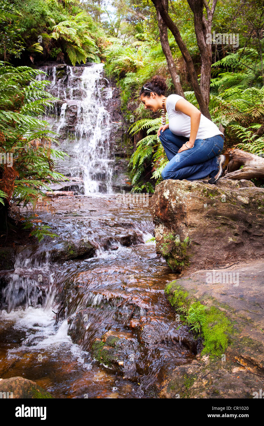 Young woman sits beside waterfall in the Blue Mountains, Australia Stock Photo