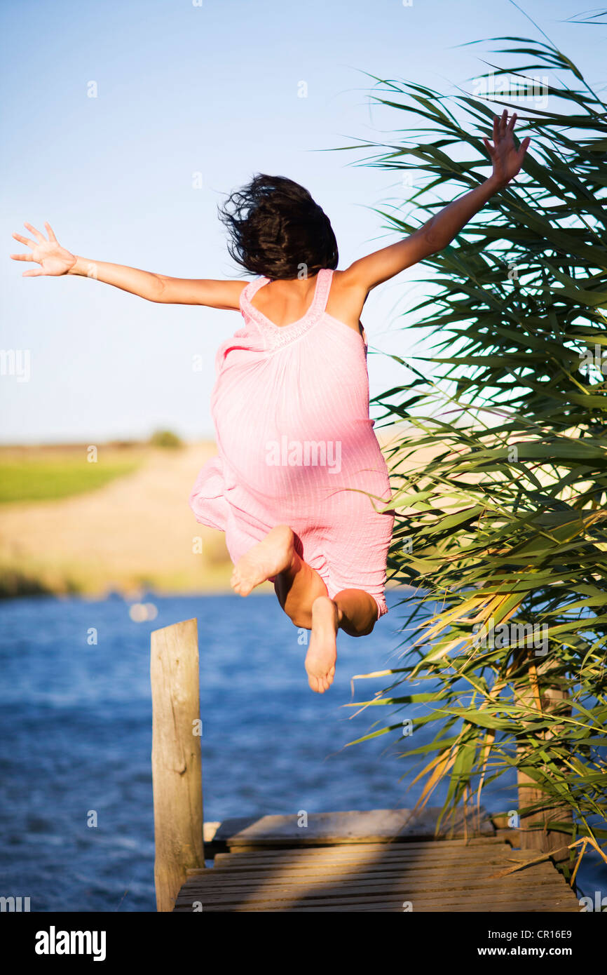 Woman jumping off dock into lake Stock Photo
