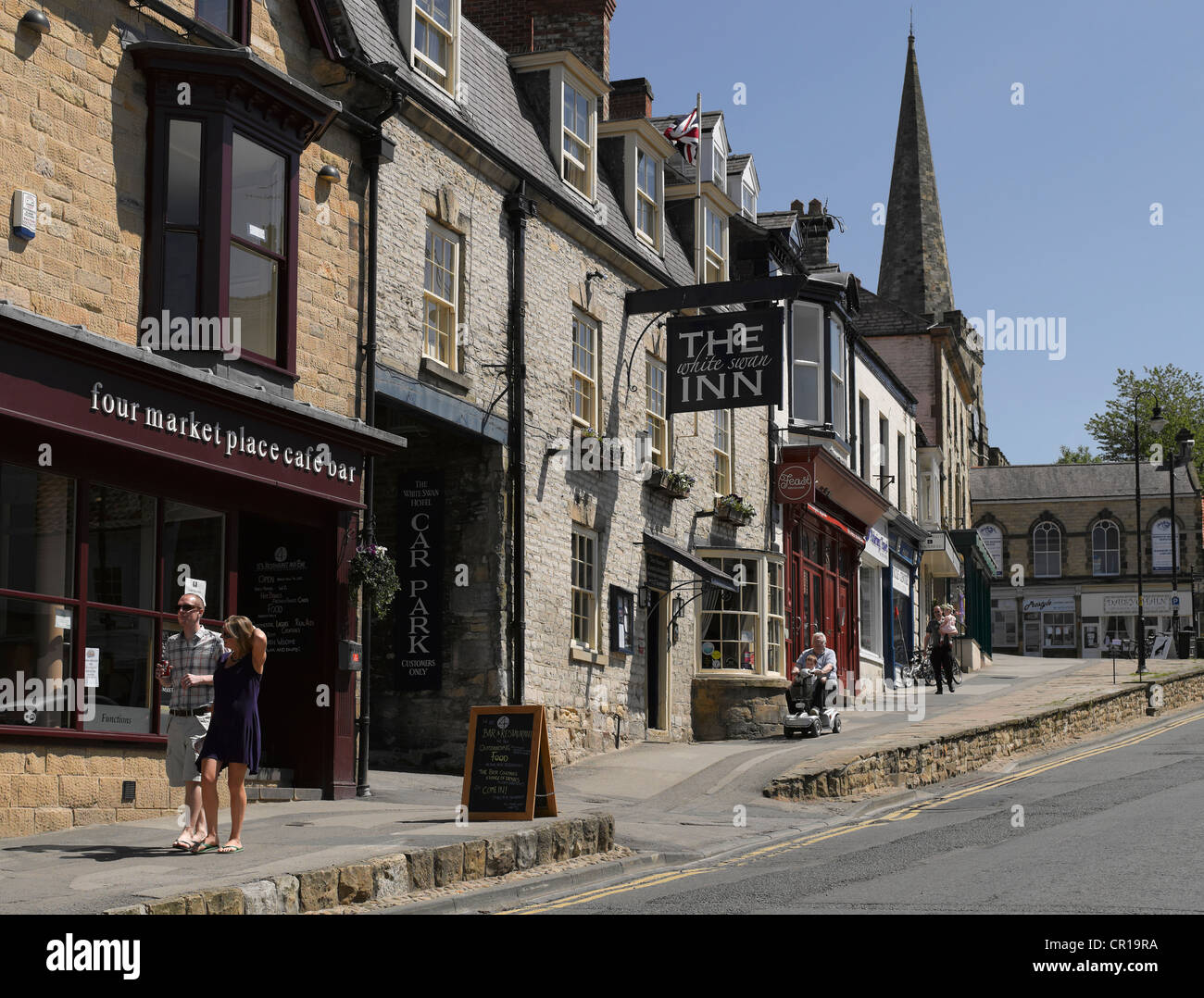 People walking in the town centre in summer Market Place Pickering North Yorkshire England UK United Kingdom GB Great Britain Stock Photo
