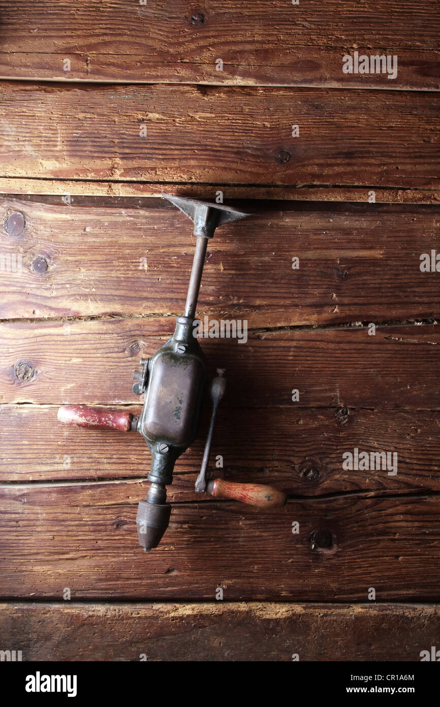 Old crank drill hanging on a rustic wooden wall Stock Photo