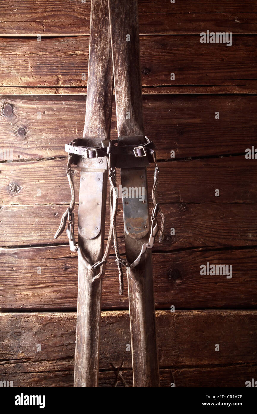 Old wooden skis with a strap binding leaning on a rustic wooden wall Stock Photo