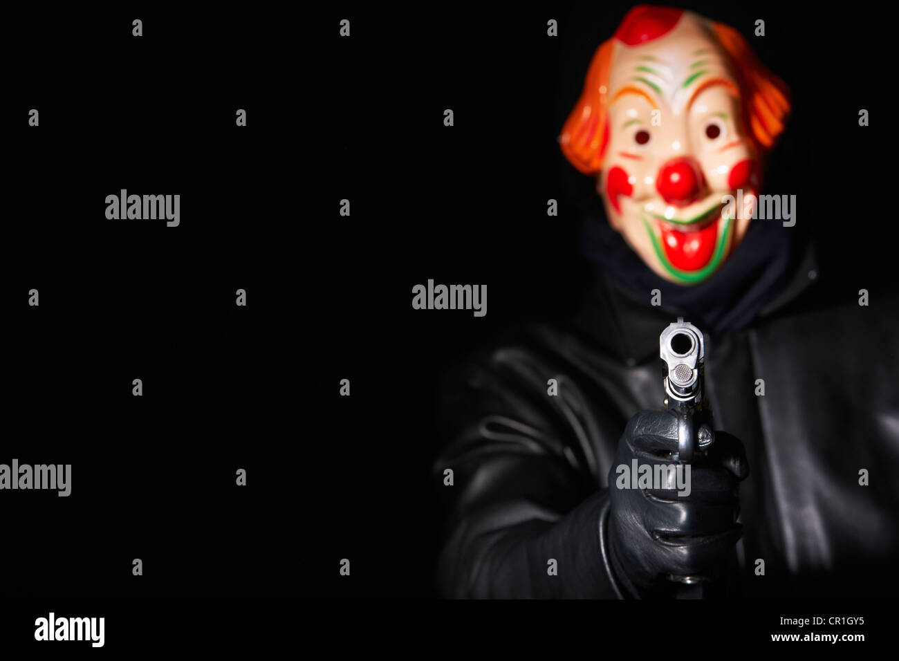 Man in clown mask pointing gun Stock Photo