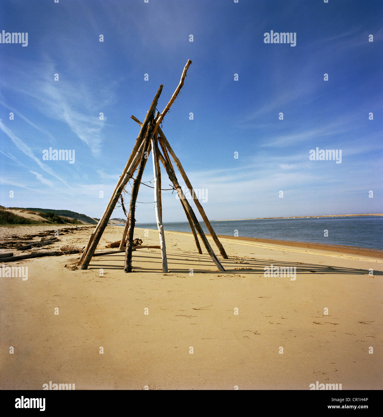 Log teepee on sandy beach Stock Photo