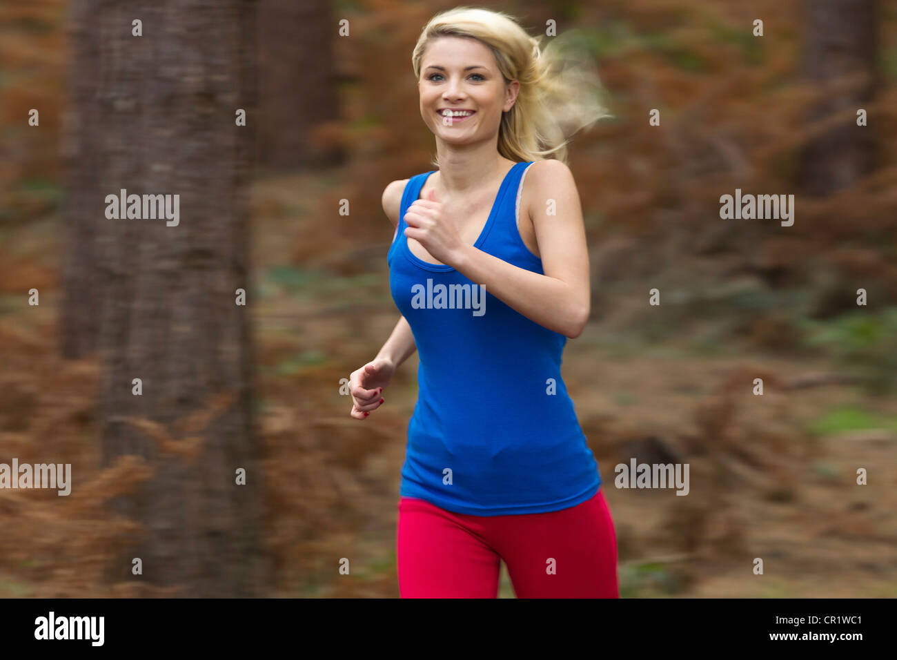 Smiling woman running in woods Stock Photo