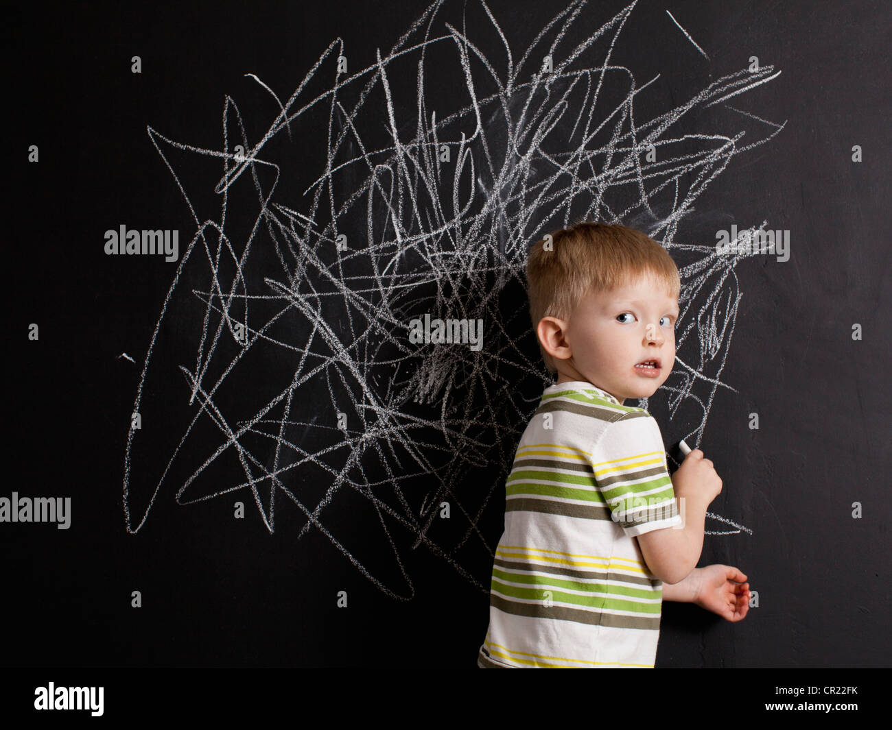 Cute toddler boy (2-3) standing against blackboard with daub written in chalk Stock Photo