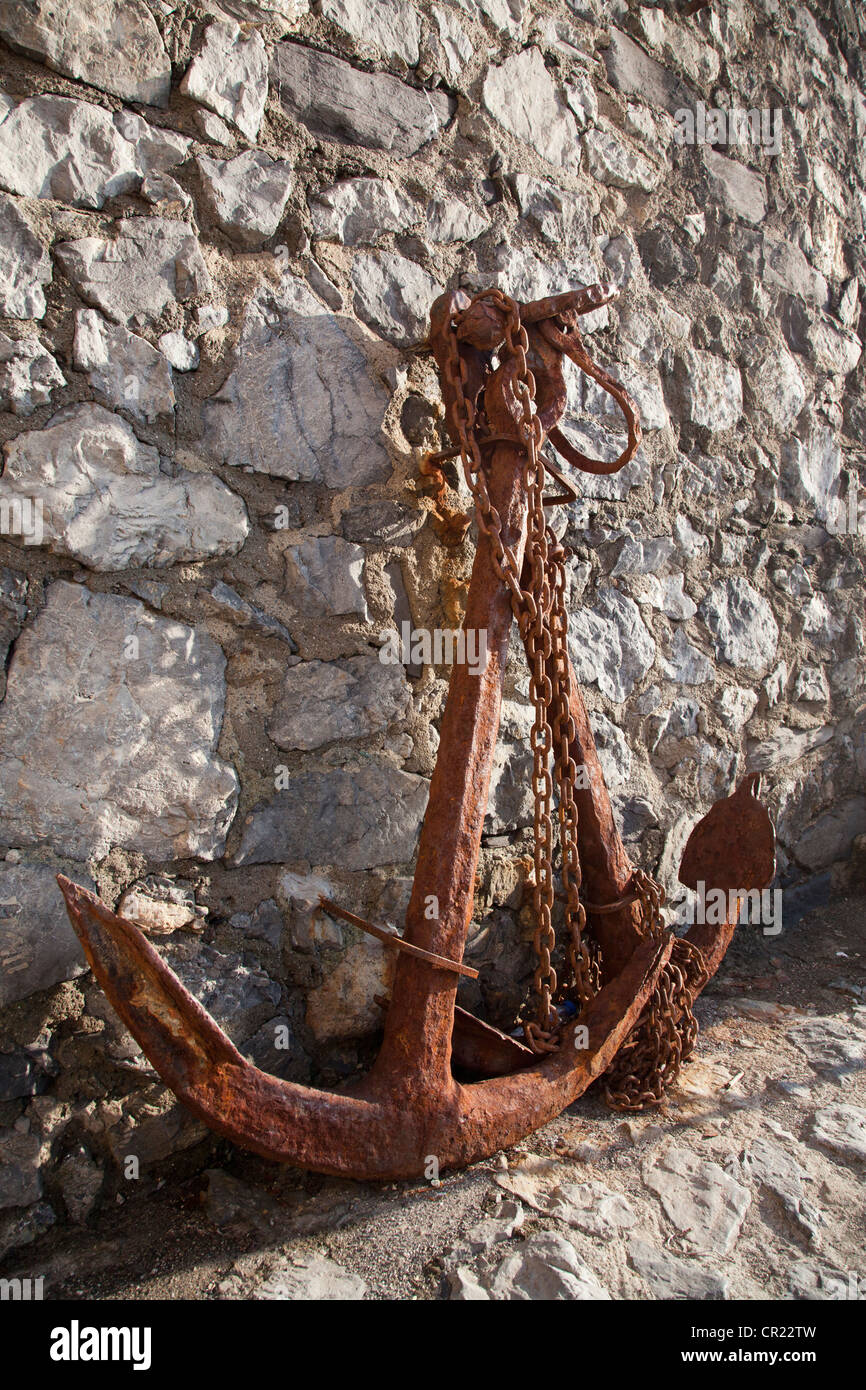 Rusted anchor against rock wall Stock Photo