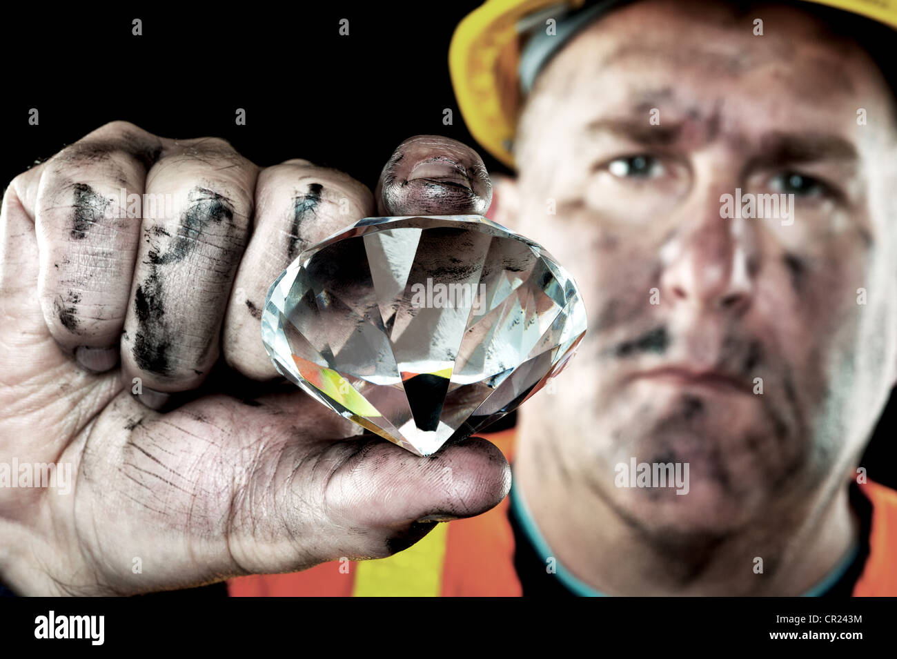 A dirty diamond miner covered in soot shows off a precious gem found in a coal mine. Stock Photo