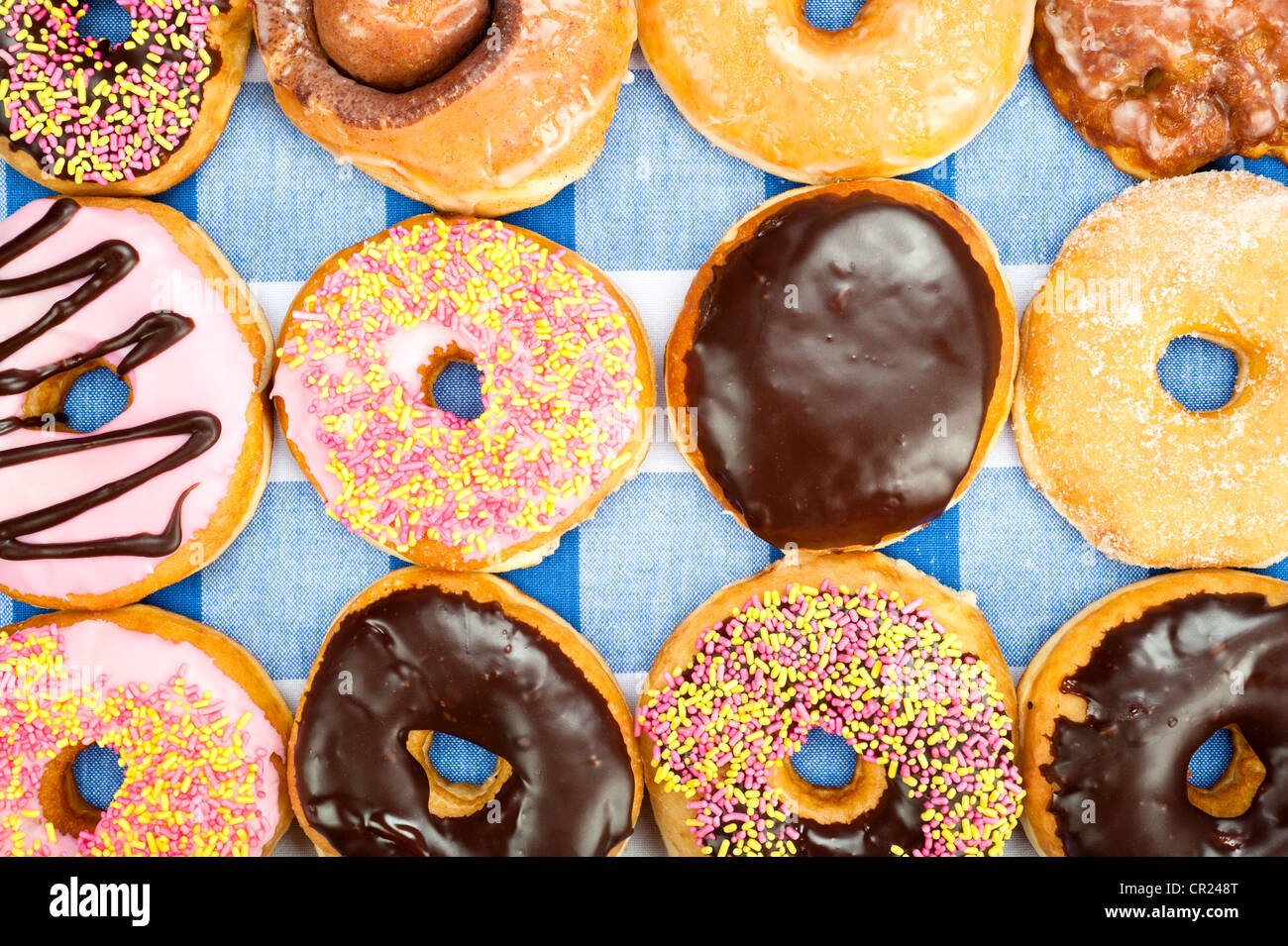 Assorted donuts with sweet toppings such as icing, sprinkles and sugary glaze on top of a blue and white checkered tablecloth Stock Photo