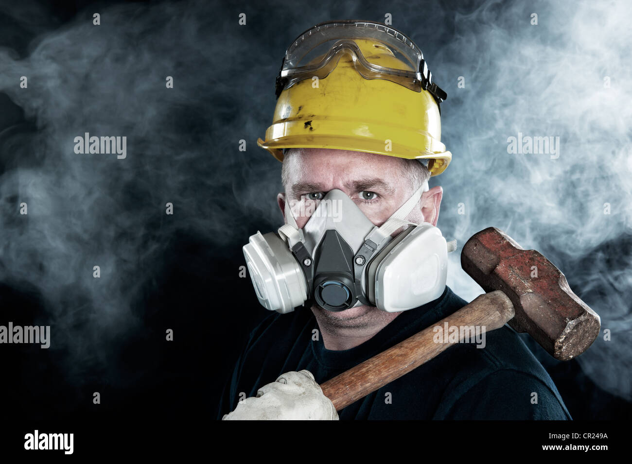 A rescue worker wears a respirator in a smoky, toxic atmosphere carrying a sledgehammer. Stock Photo